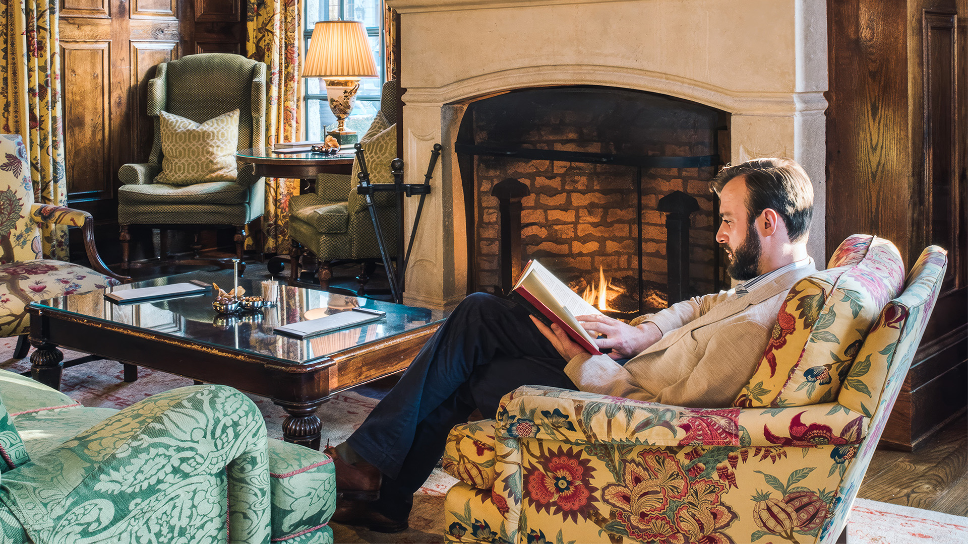 a man sitting in a chair reading a book by a fireplace