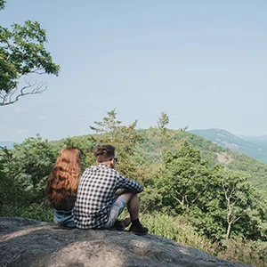 a man and woman sitting on a rock looking at a valley