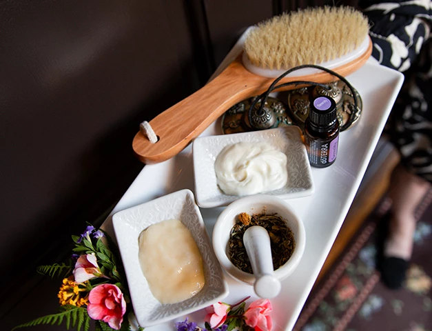 a white tray with a wooden brush and bowls of cream and a small bowl of green leaves