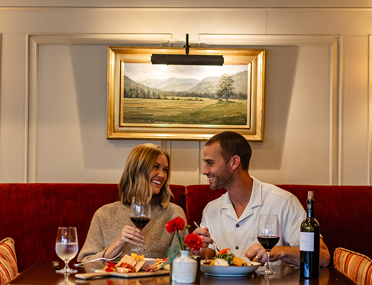 a man and woman sitting at a table with food and wine