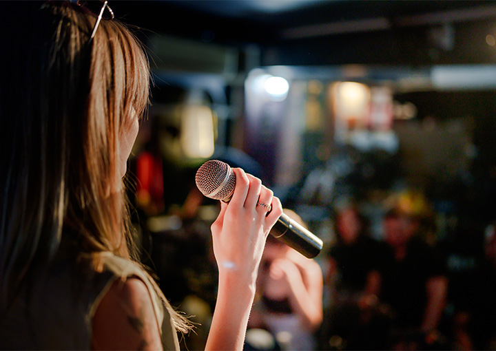 a brunette woman wearing sunglasses holding a microphone in front of a crowd