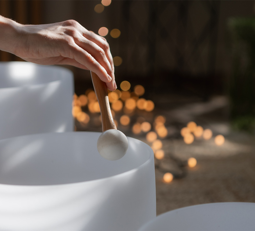 a hand holding a stick over a sound bath drum