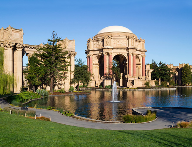 A large building with a dome and columns beside a lake with a fountain.
