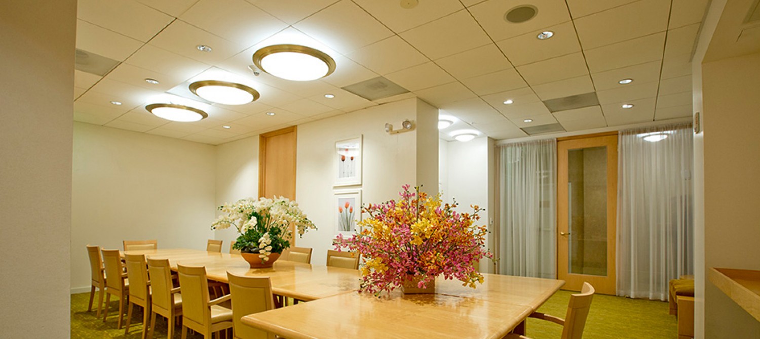 A brightly lit meeting room with a long wooden table, chairs, and floral arrangements.