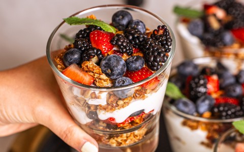 a hand holding a glass of fruit parfait