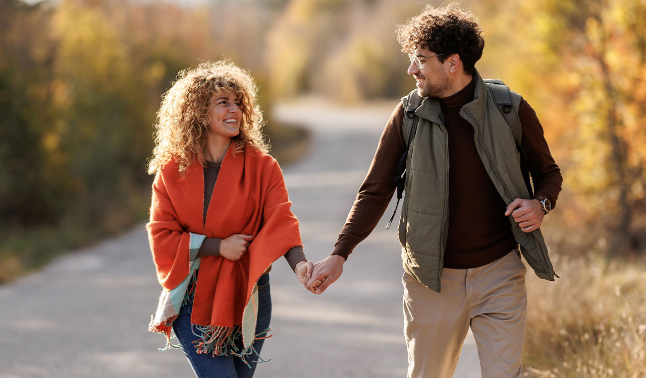 a man and woman holding hands and walking on a road