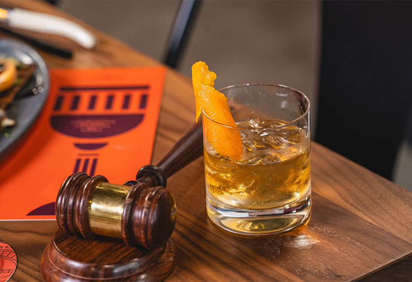 a glass of alcohol with an orange peel on top of a wooden gavel