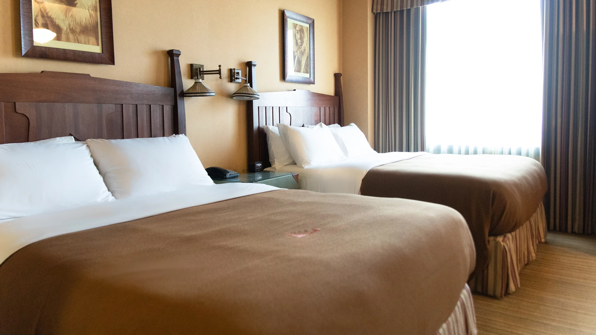 A hotel room with two double beds, wooden headboards, and a window with curtains.