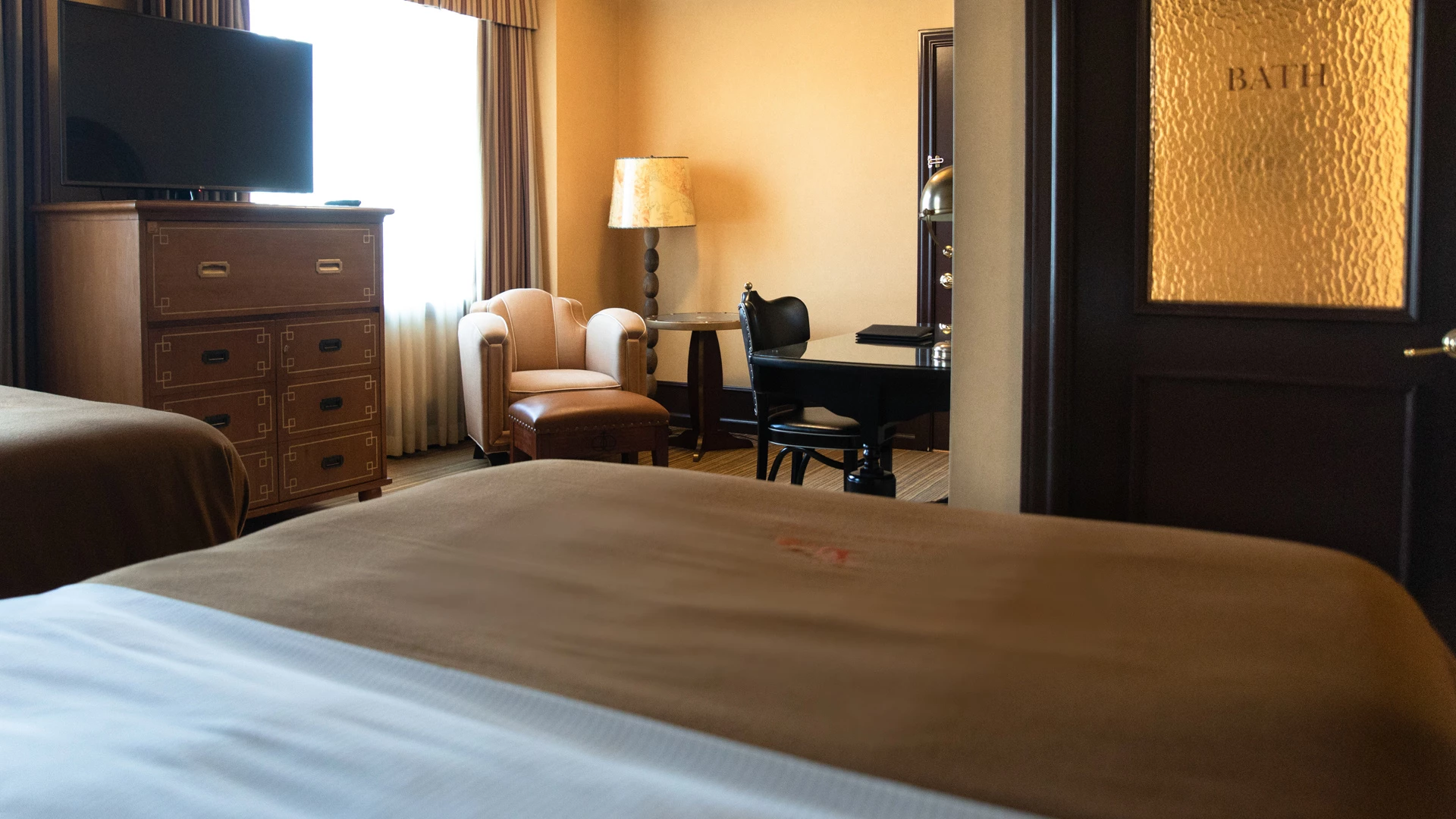 A hotel room with two beds, a desk, chair, TV, and dresser.