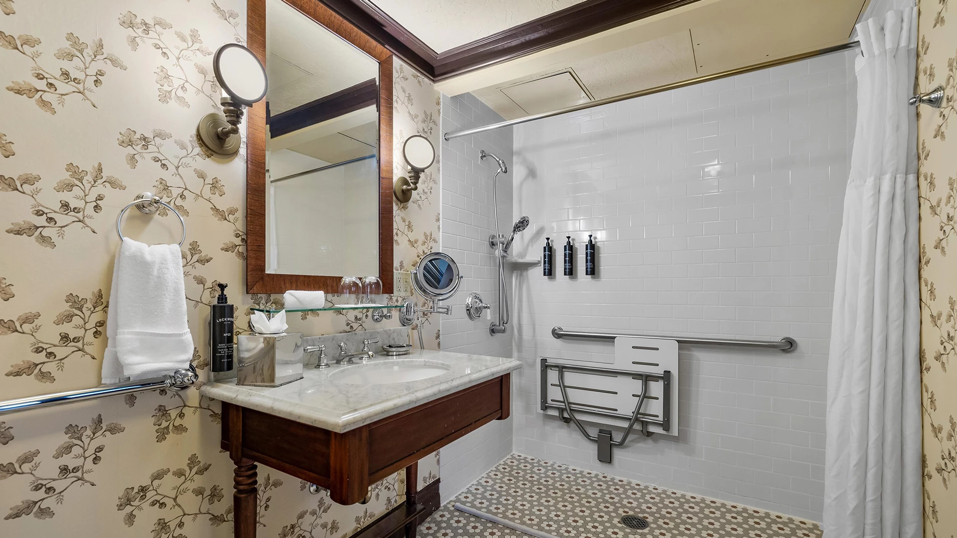 A bathroom with a marble countertop, wooden vanity, white sink, shower, and toiletries.