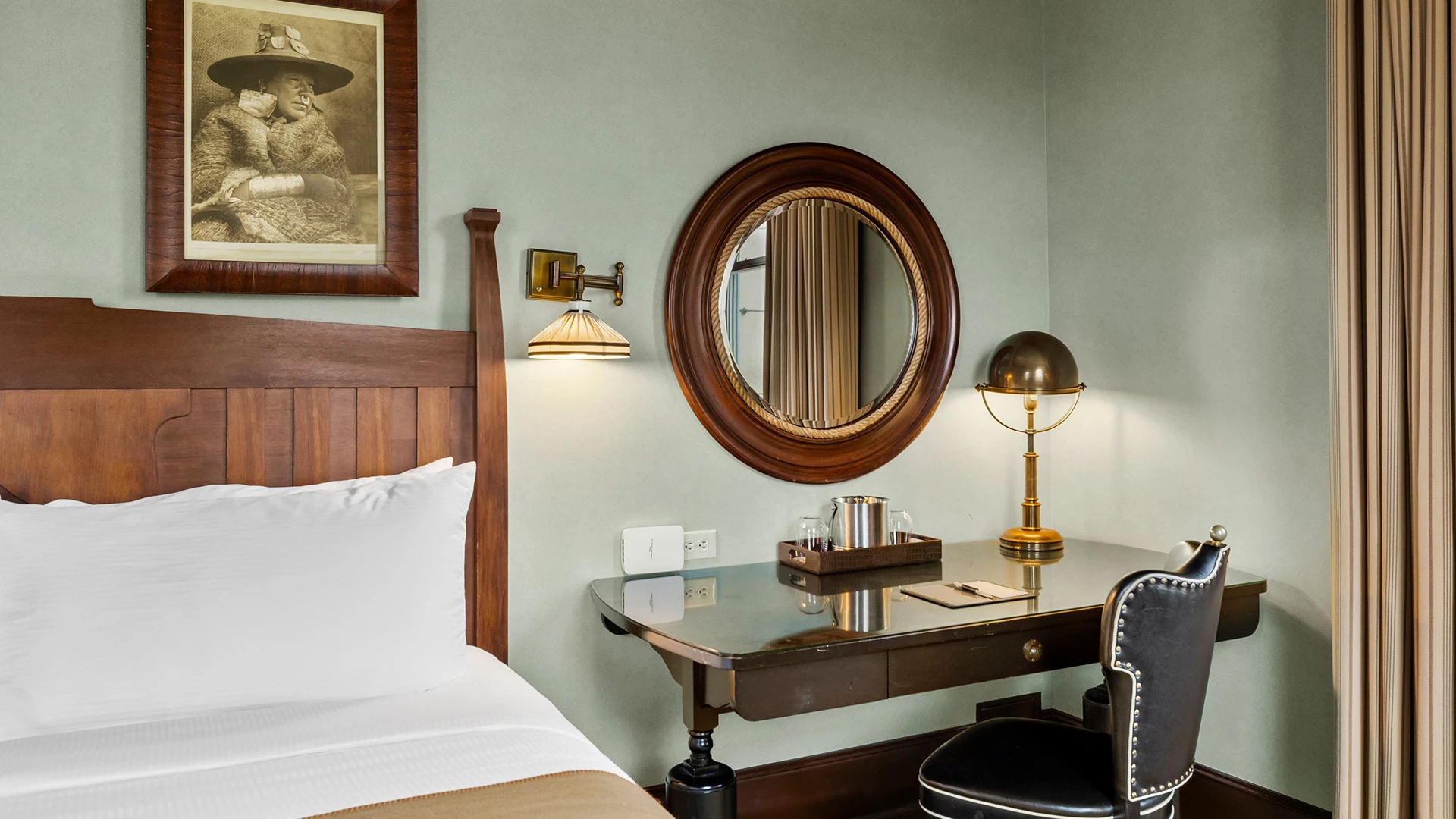 A hotel room with a bed, desk, chair, mirror, and lamp.