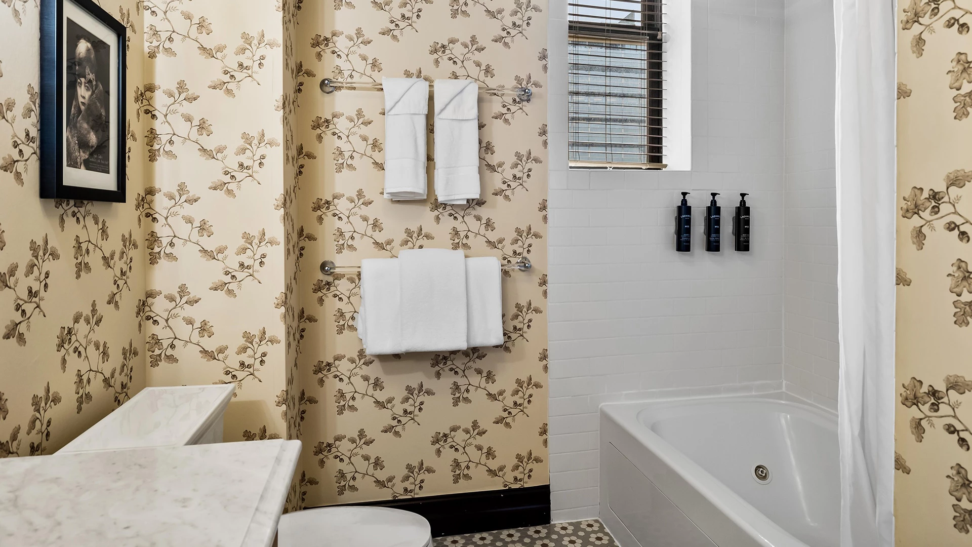 A clean bathroom with a tub, toilet, sink, and floral wallpaper