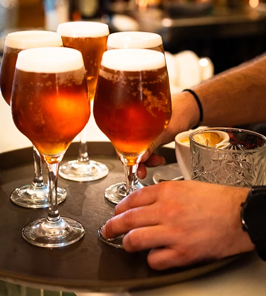 a hand holding a tray of glasses of beer