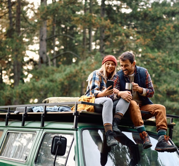 a man and woman sitting on top of a car planning their autumn road trip at all 14 oxford suites locations along the west coast
