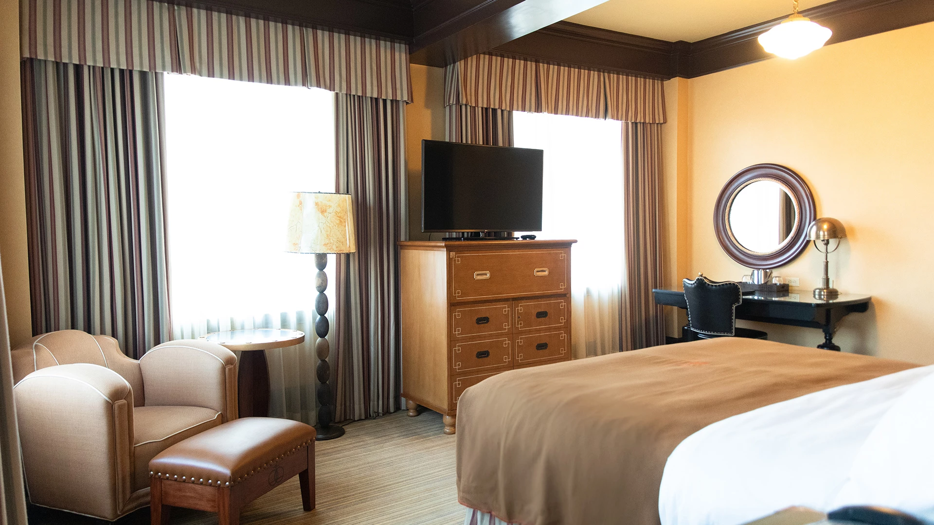 A wide view of a hotel room with a bed, dresser, chair, and TV.