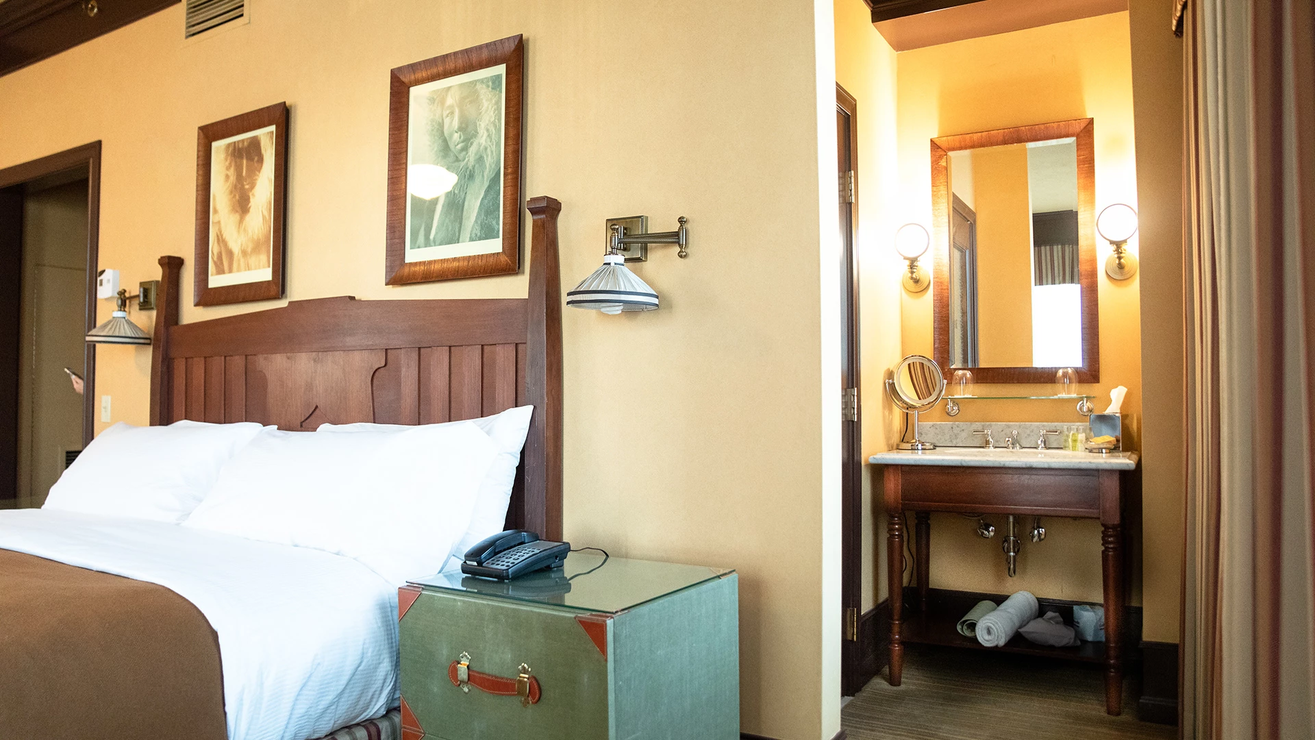 A hotel room with a bed, nightstand, and bathroom with sink and mirror.