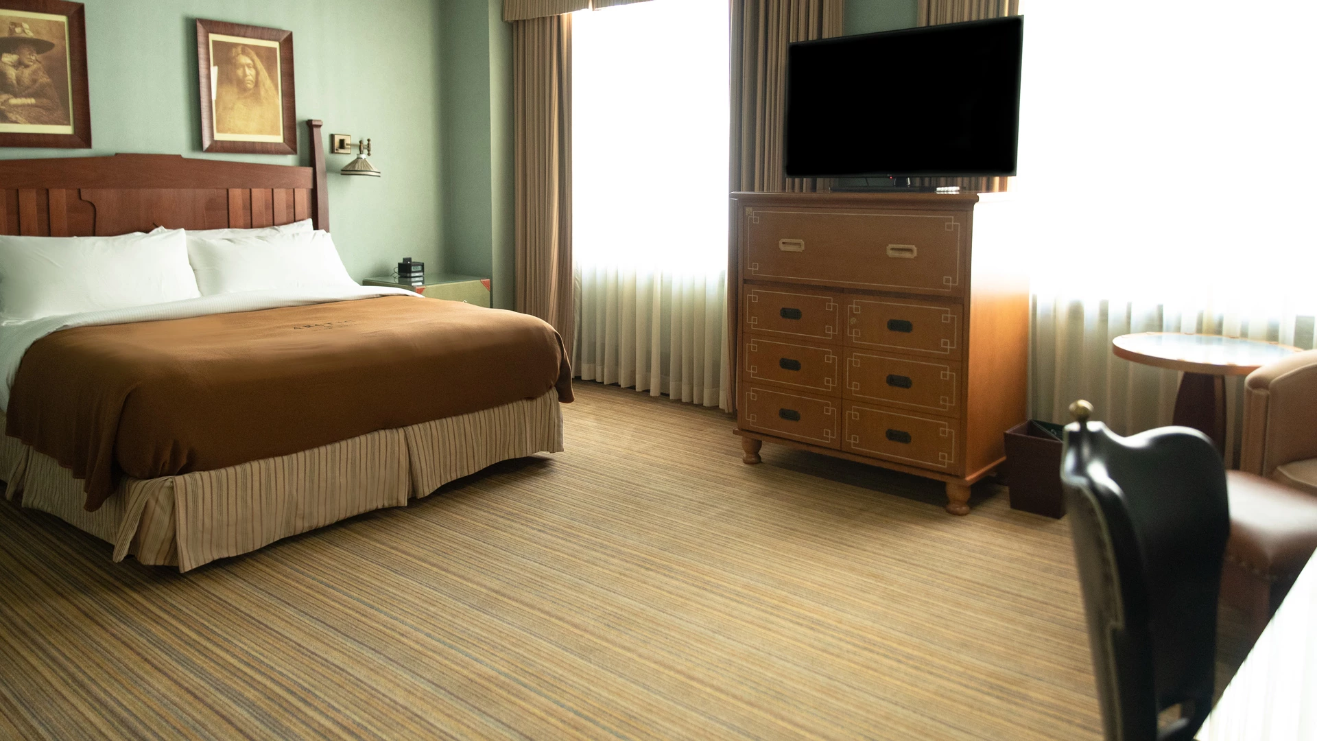 A wide view of a hotel room with a bed, dresser, TV, and chair.