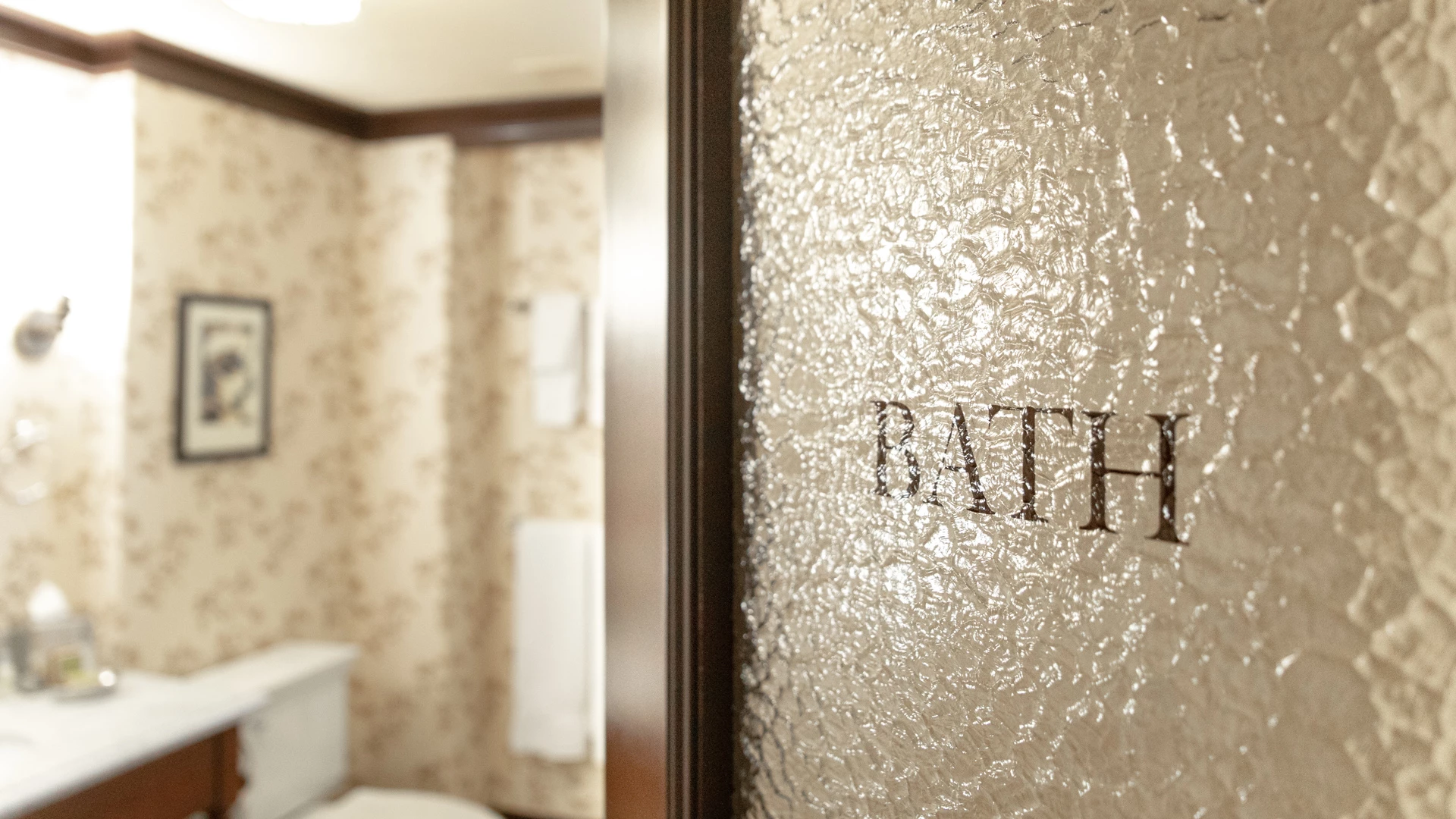 a bathroom with a textured glass door and a floral wallpaper