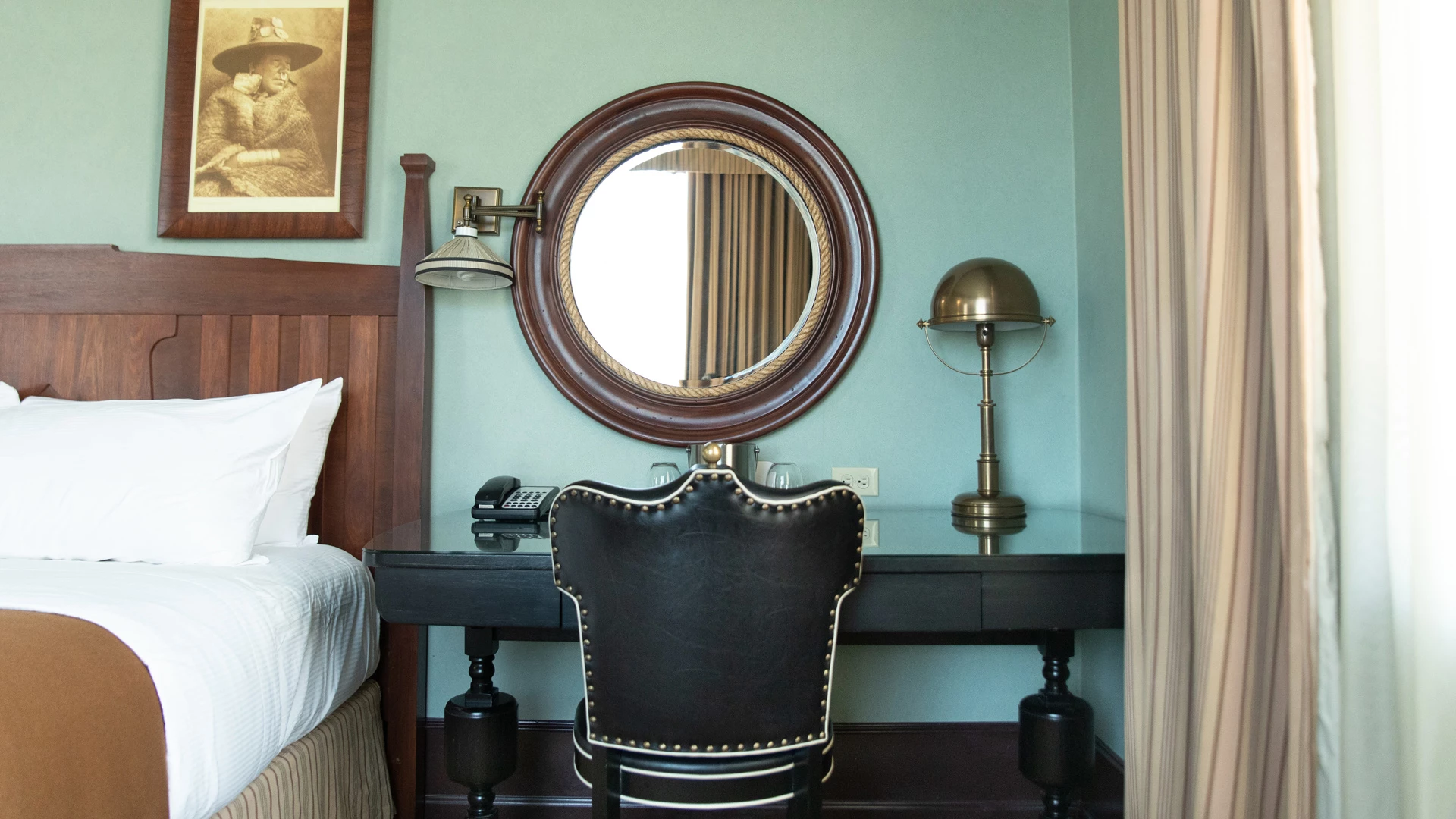 A hotel room with a bed, desk, chair, mirror, and lamp.