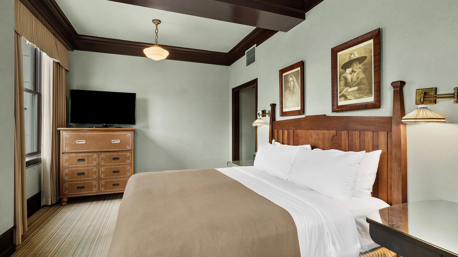 A hotel room with a bed, dresser, TV, and window.