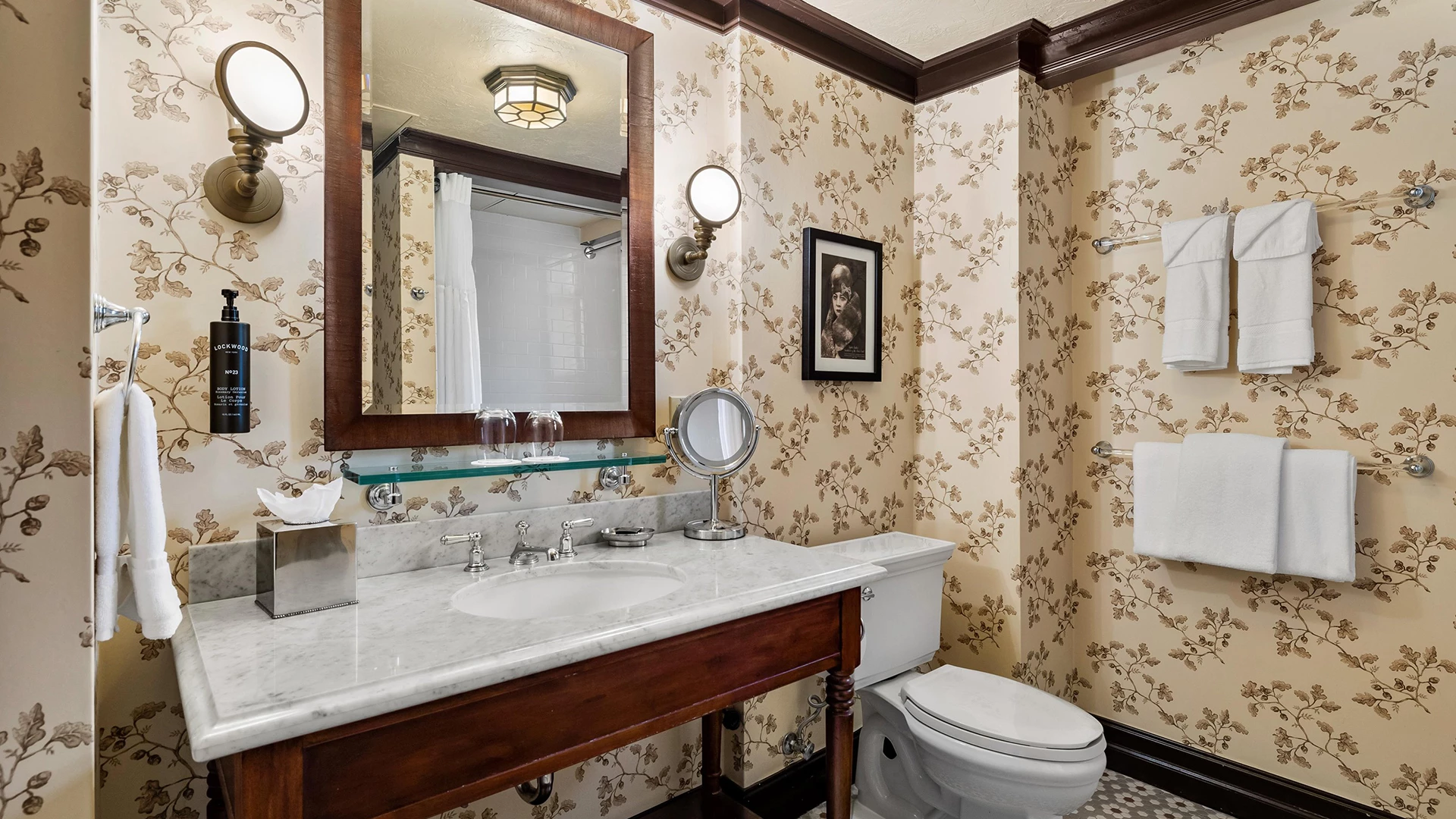 A bathroom with a marble countertop, wooden vanity, and floral wallpaper.
