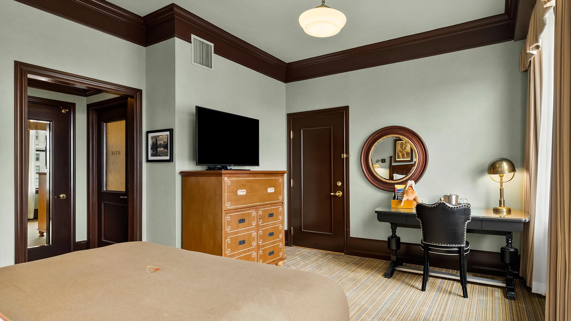 A wide-angle view of a hotel room with a bed, dresser, desk, and TV.