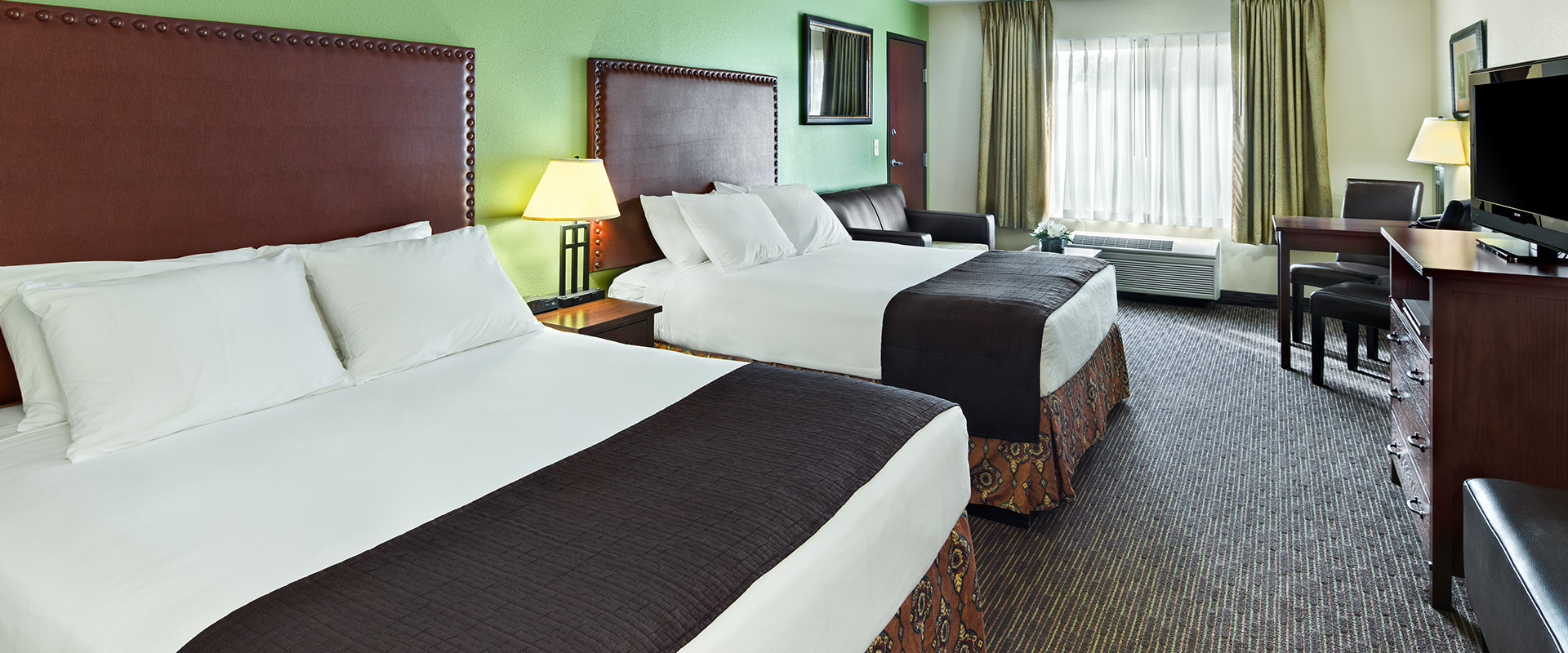 A hotel room with two beds, a desk, and a window