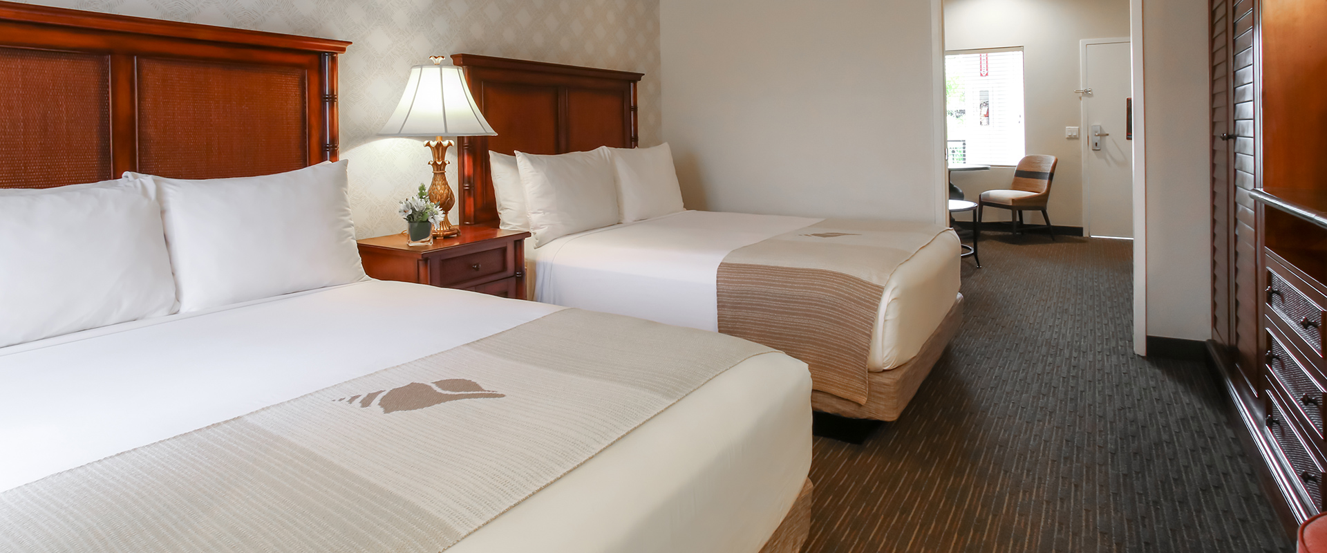 A hotel room with two beds, a nightstand, and a lamp.