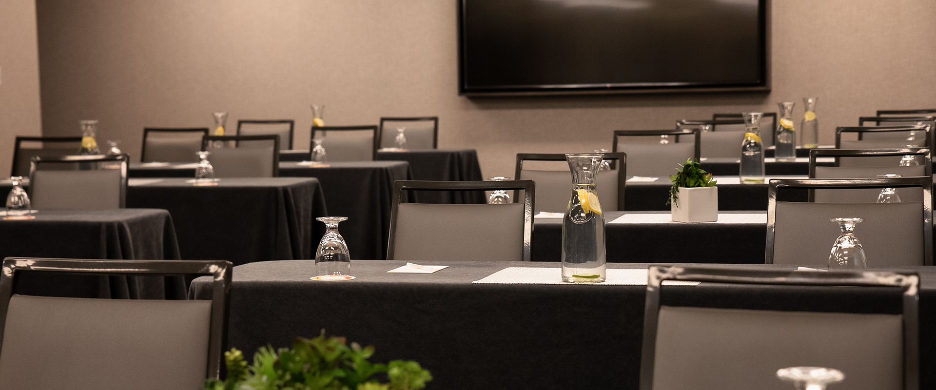 a room with chairs and tables with black tablecloths and a vase with water