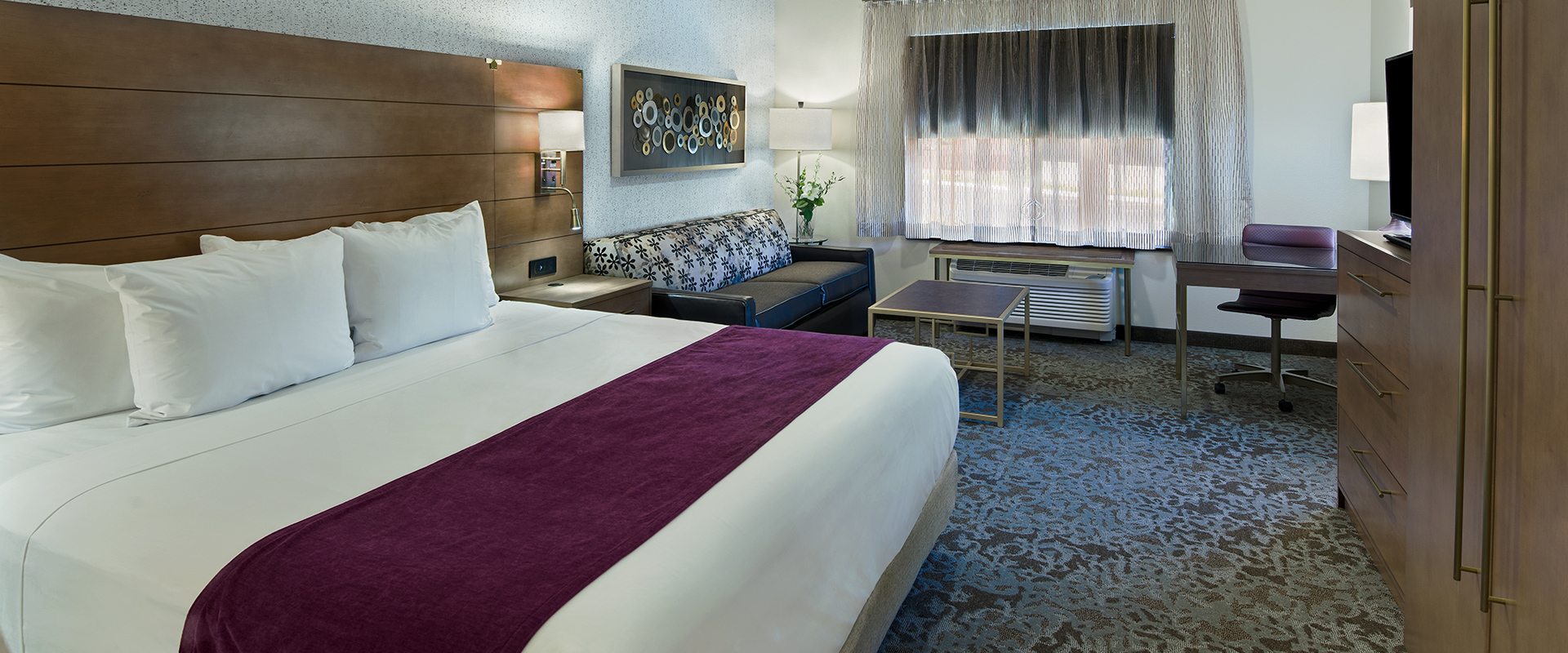 A wide view of a hotel room with a king-size bed, sofa, desk, TV, and dresser.