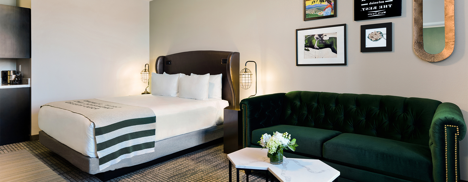 A hotel room with a bed, green velvet sofa, coffee table, and artwork on the wall.