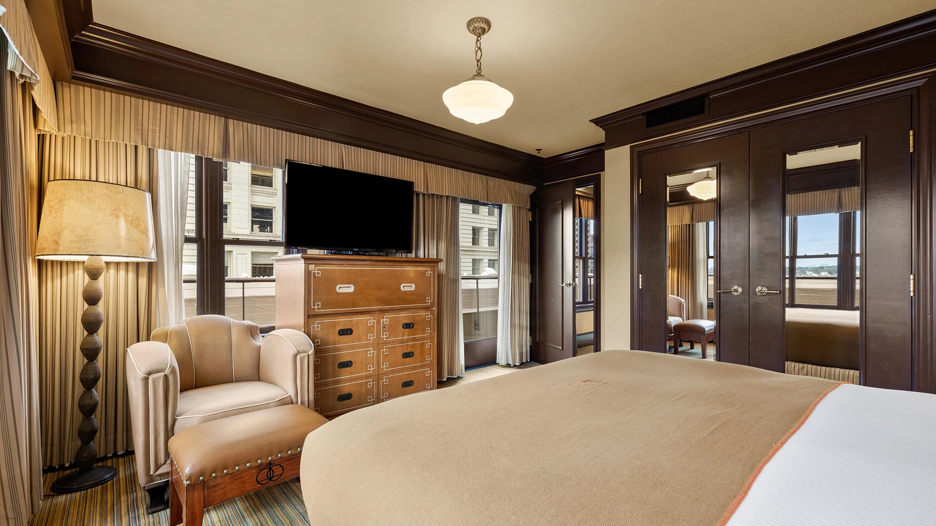 A hotel room with a bed, chair, dresser, lamp, TV, and door.