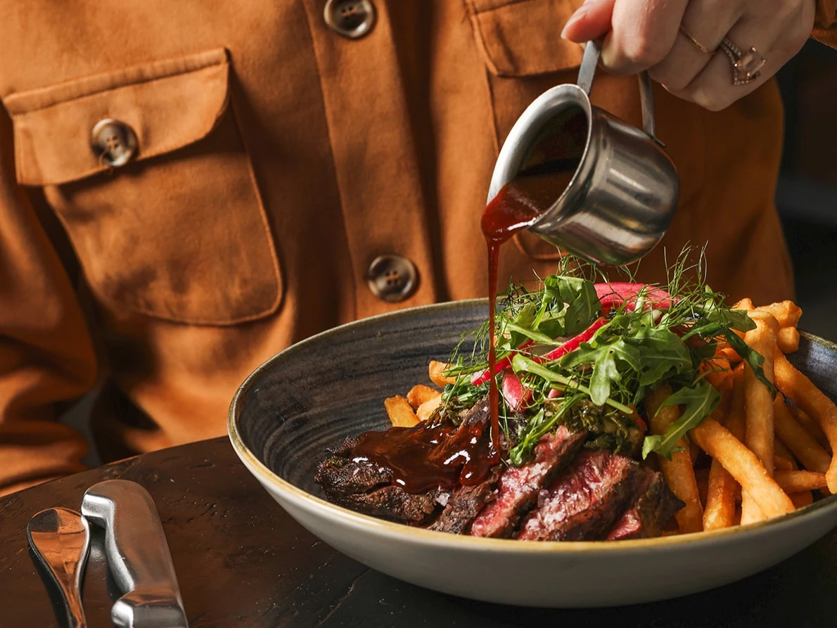 a person pouring sauce into a bowl of food