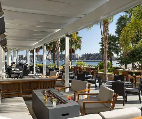 a room with tables and chairs and a body of water in the background