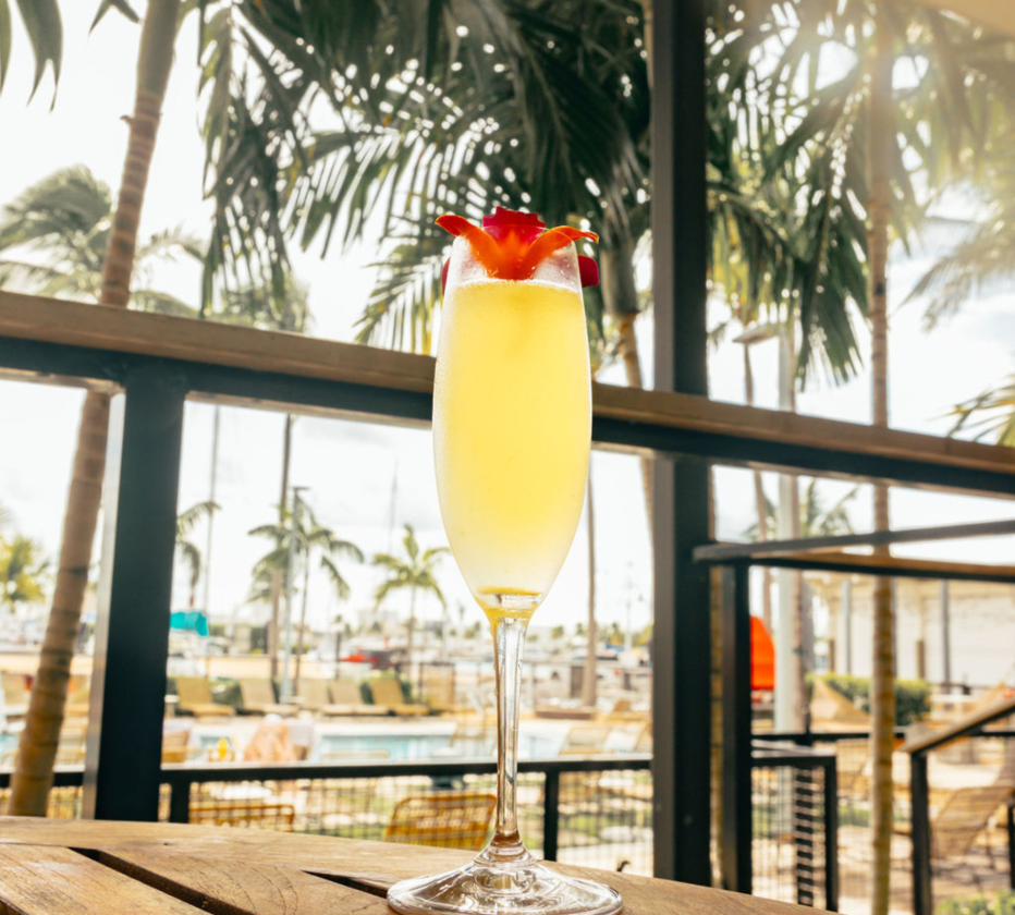 a glass of yellow liquid with a red flower on top of it