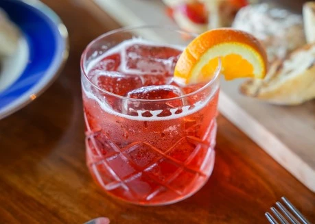 a glass of red liquid with a slice of orange on top