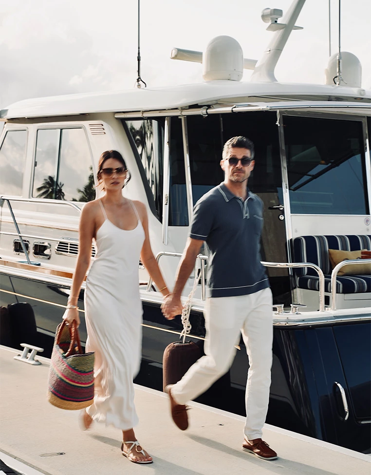 a man and woman holding hands and walking on a dock with a boat