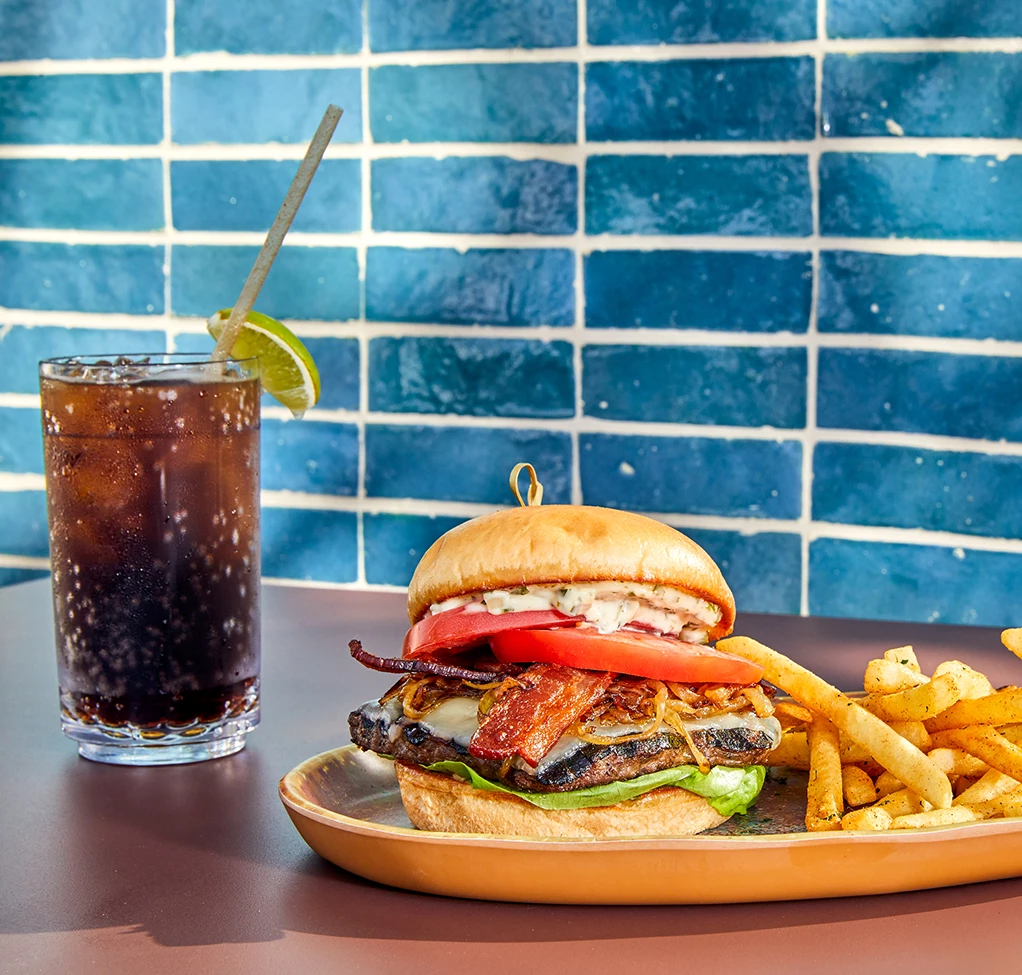 a plate of burger and fries with a drink in the background