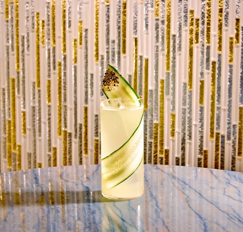 a glass of liquid with cucumber slice on top