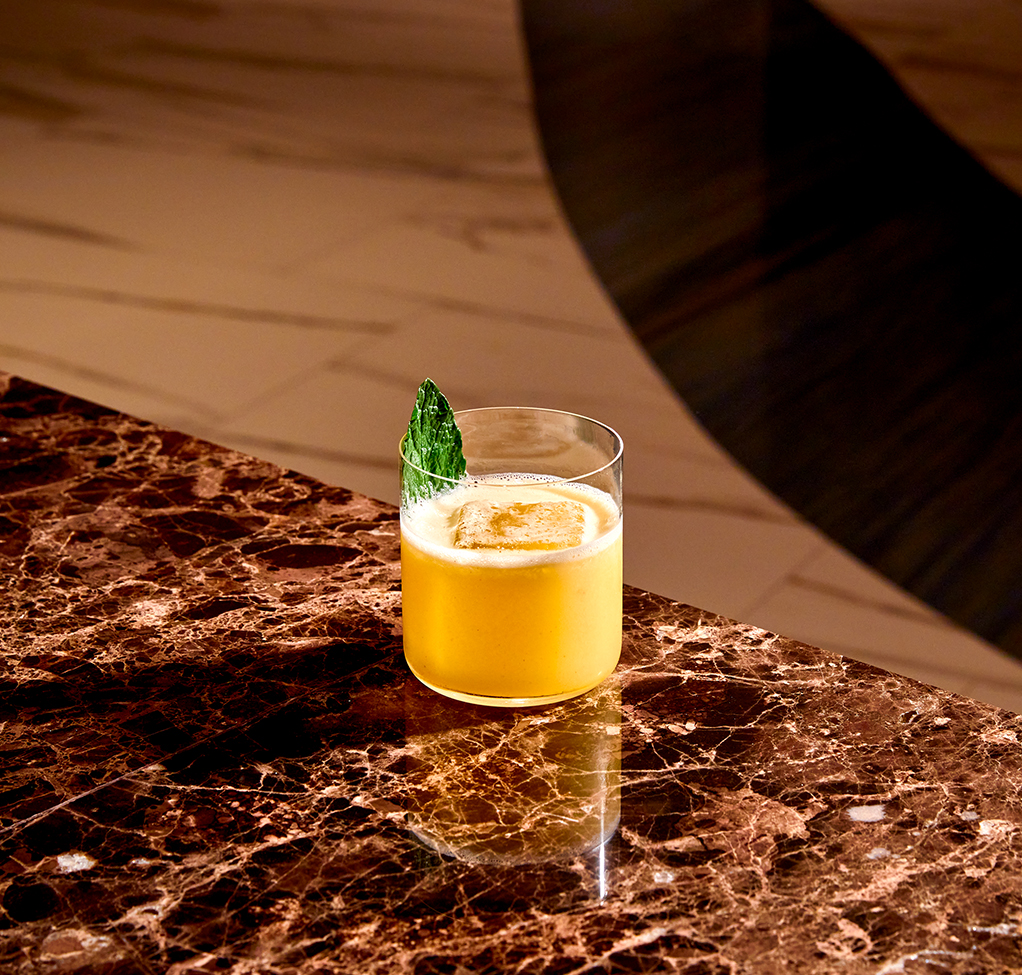 a glass of yellow liquid with a leaf on a marble surface