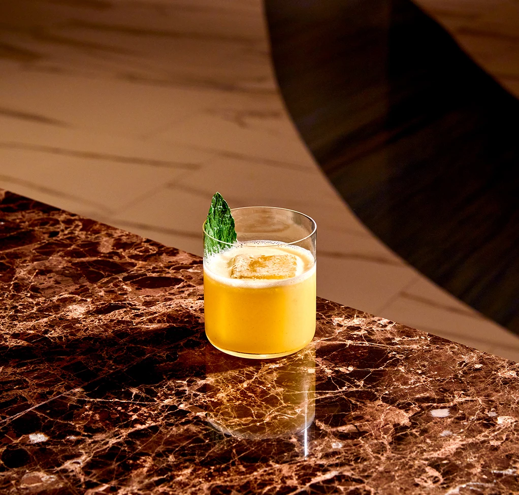 a glass of yellow liquid with a leaf on a marble surface