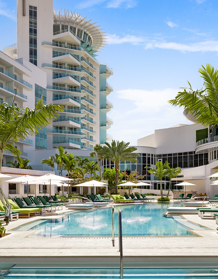 a pool with lounge chairs and umbrellas in front of a building