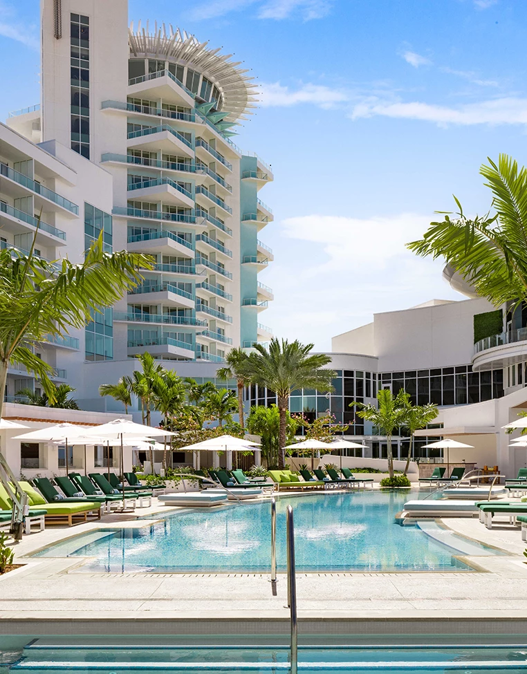 a pool with lounge chairs and umbrellas in front of a building