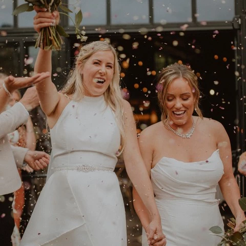 2 brides walking out of the ceremony being showered with confetti