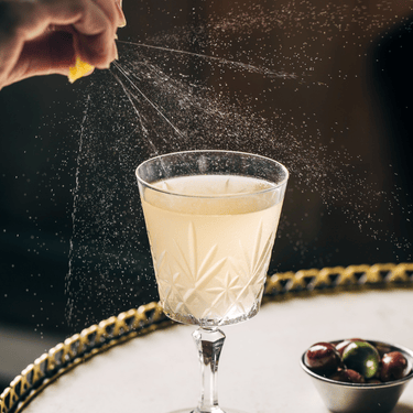 a hand spraying a lemon into a glass of liquid