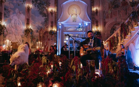 a man playing guitar in a room with flowers and candles