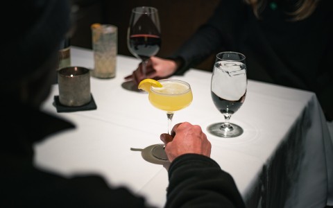 a hand holding a glass of yellow liquid with a lemon wedge