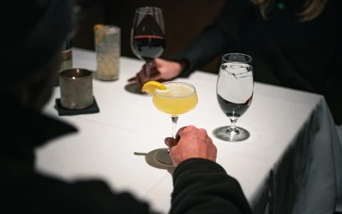 a hand holding a glass of yellow liquid with a lemon wedge