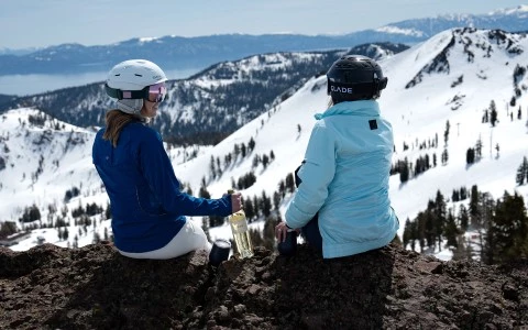 two women sitting on a mountain with snow covered mountains