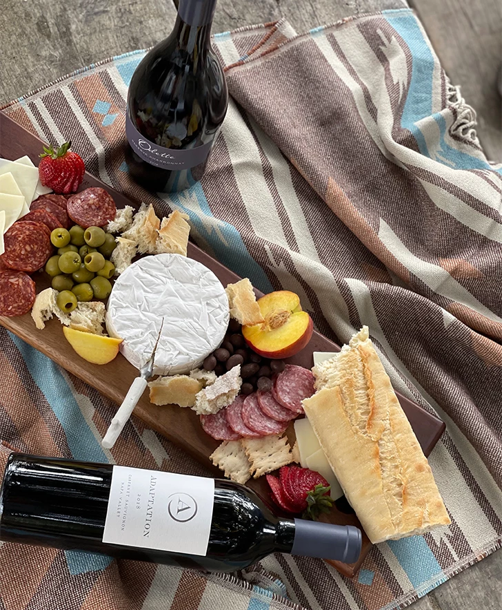a cheese and fruit on a wooden board next to a bottle of wine